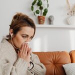 Woman sneezing into a tissue outdoors among spring blossoms during allergy season
