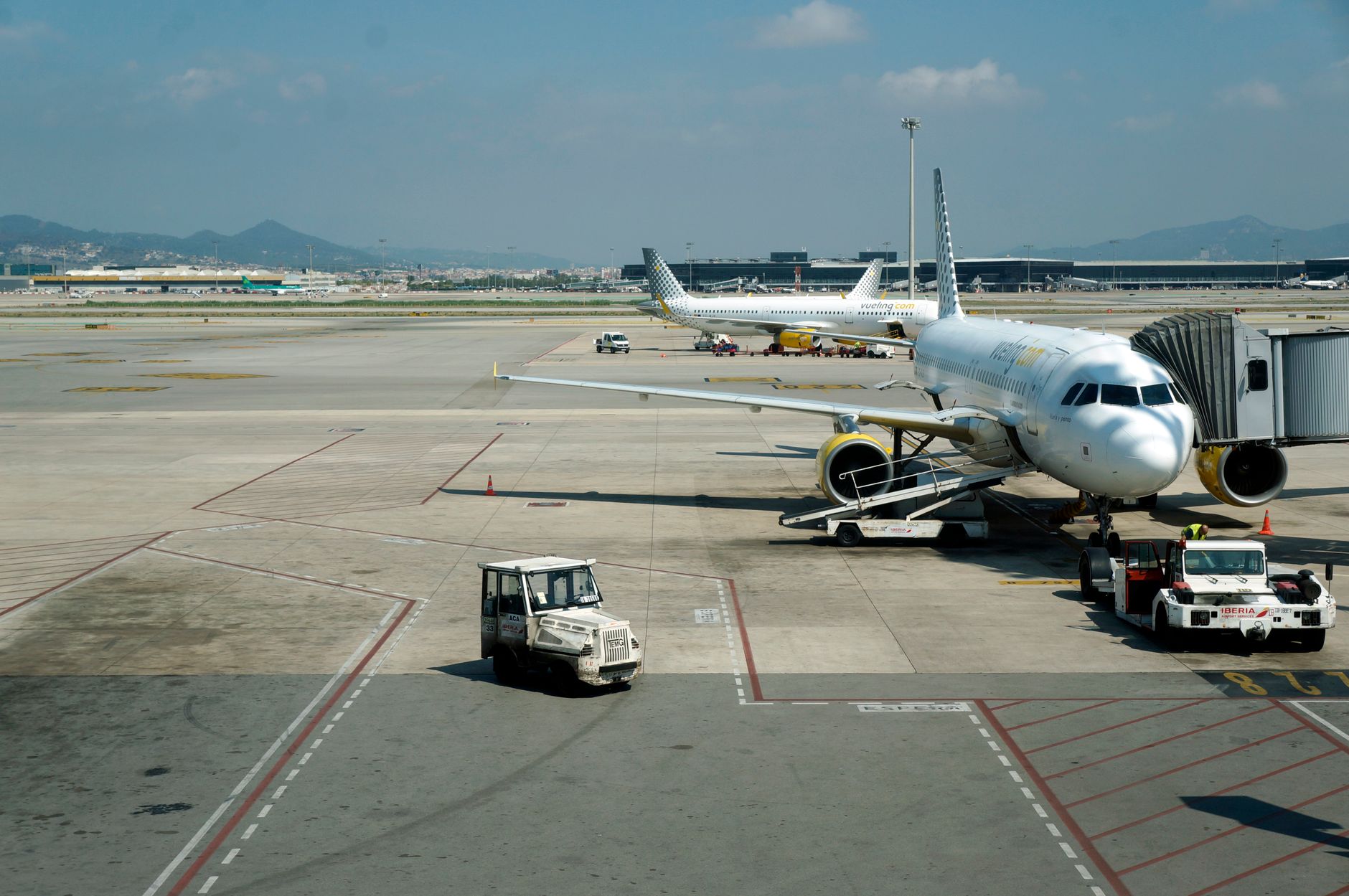 A commercial airplane prepares for boarding at Girona Airport with clear skies and mountains in the distance, illustrating A layover is the biggest single discount you can choose
