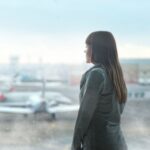 A woman gazing at airplanes through a window at Kyiv's airport terminal, capturing a moment of reflection, illustrating The Cheapest Time to Fly Is the Next Six Weeks, and Booking on a Tuesday Won't Help