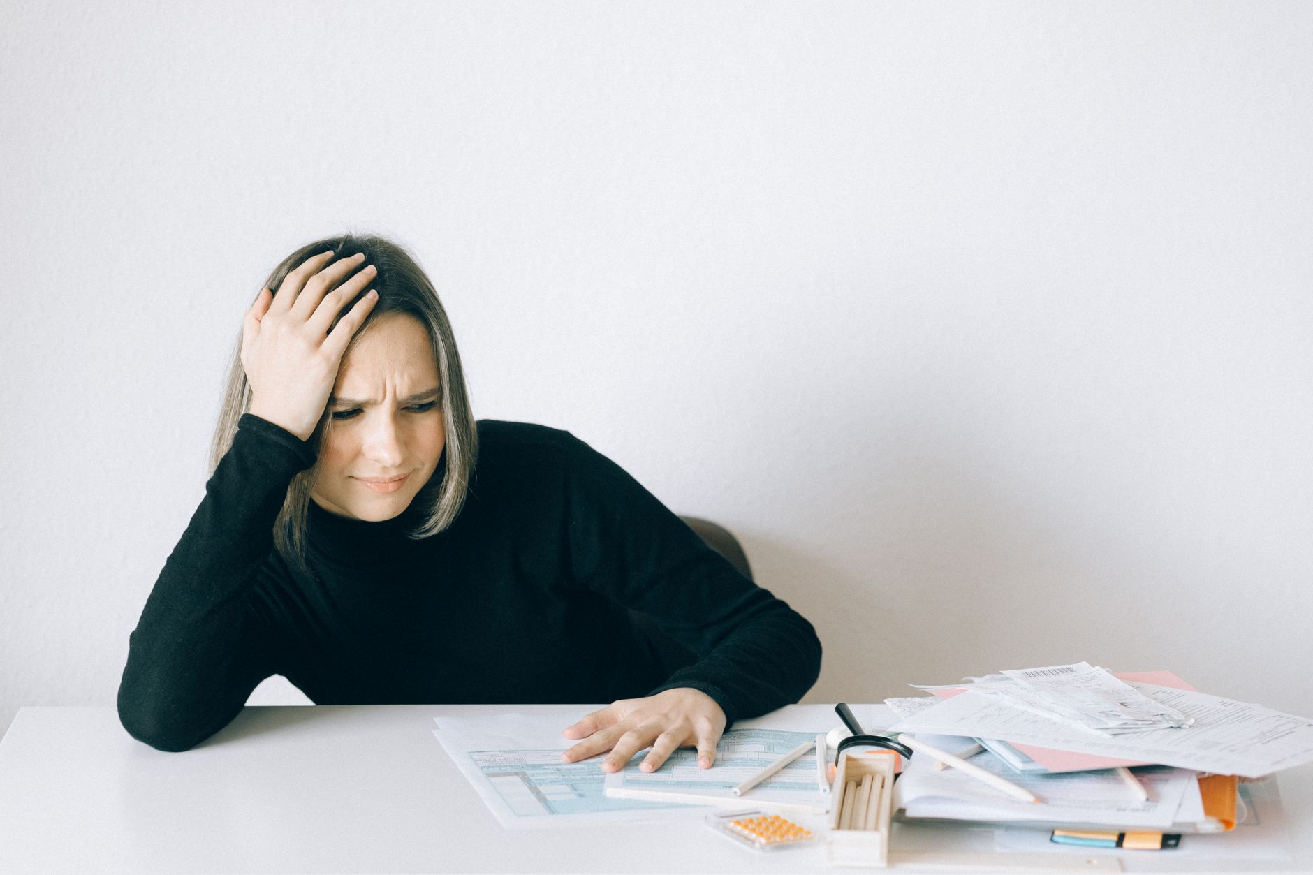 Woman in black sweater stressed with financial paperwork, overwhelmed at white table, illustrating Small raise gaps compound into a real number