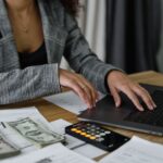 A businesswoman working on finance management with cash and calculator on desk, illustrating The Gender Pay Gap Opens After Your First Job: A $37,956 Lesson for Equal Pay Day