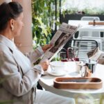 An elegant woman reads a newspaper at an outdoor cafe, enjoying a relaxing morning, illustrating How to Create a Self-Care Sunday Routine: 10 Relaxing Rituals to Reset Your Week