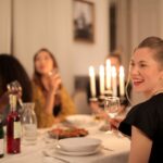 Group of diverse women enjoying a candle-lit dinner, smiling and chatting, illustrating How to Host the Perfect Dinner Party: Menu Planning, Table Setting, and Entertainment Tips