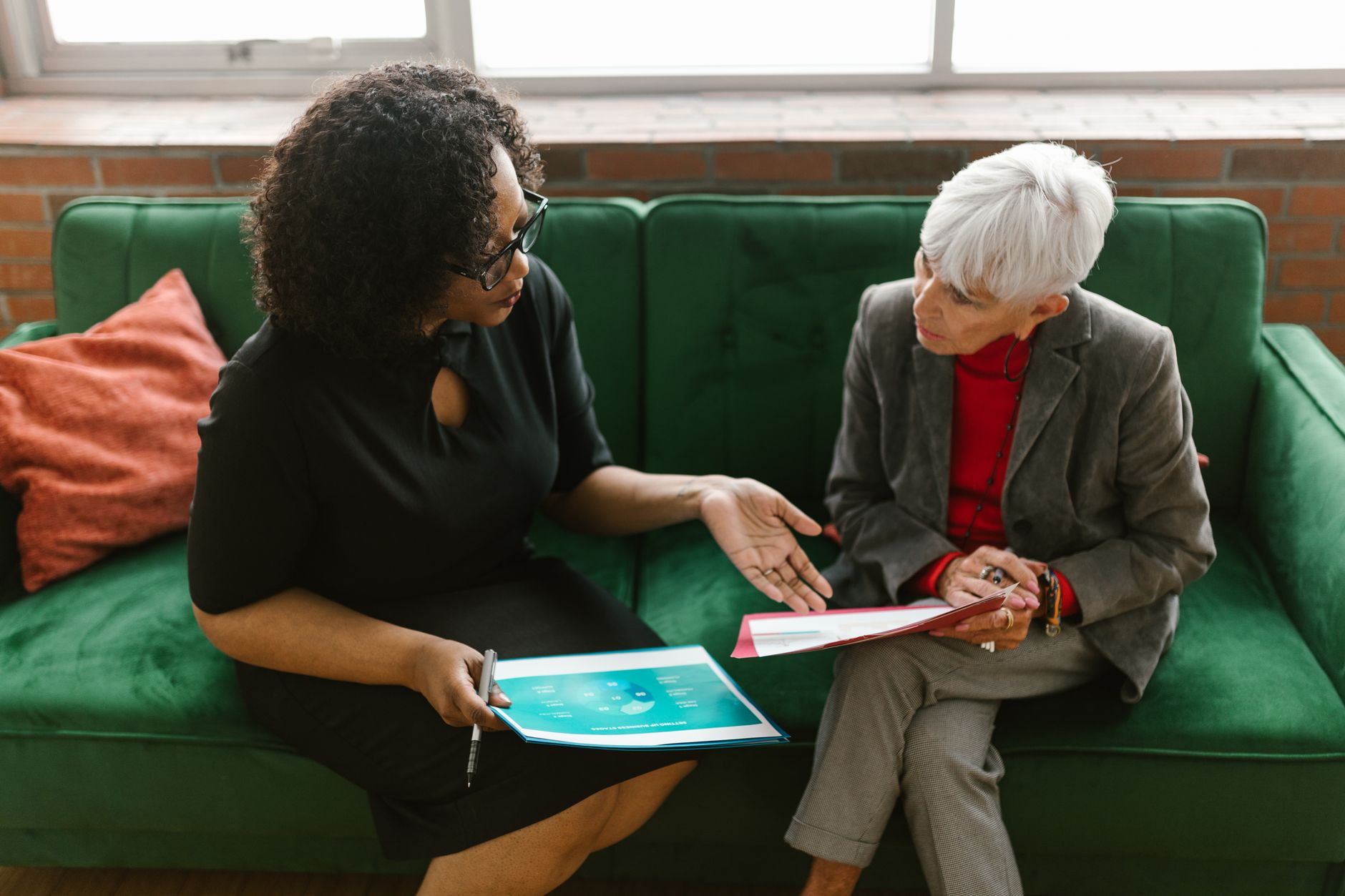 Two women in a business meeting discuss documents while sitting on a green sofa, illustrating Master the Actual Conversation