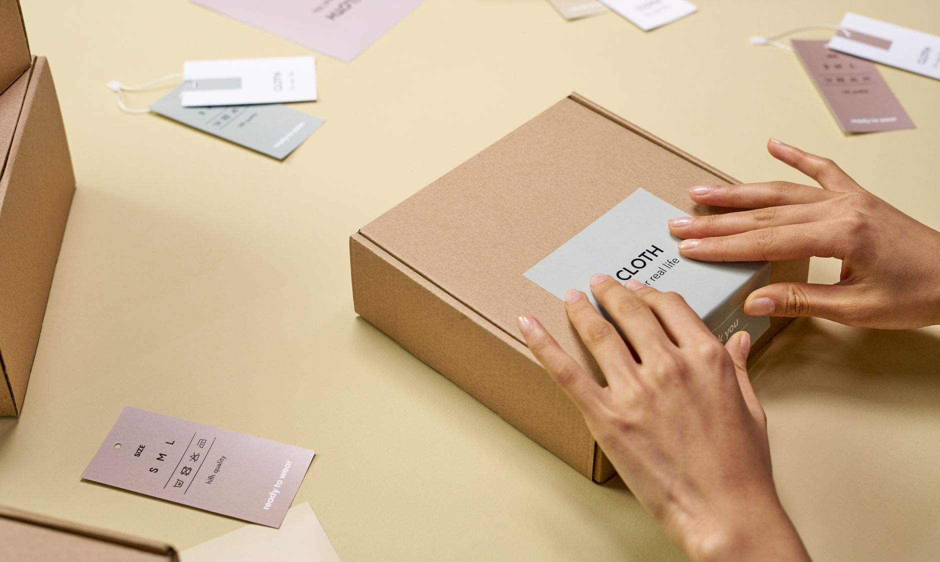 Hands carefully packing a cardboard box with multiple tags around, emphasizing sustainable packaging, illustrating E-commerce and Handmade Goods