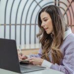 Woman taking notes beside her laptop while drafting a performance review self-assessment