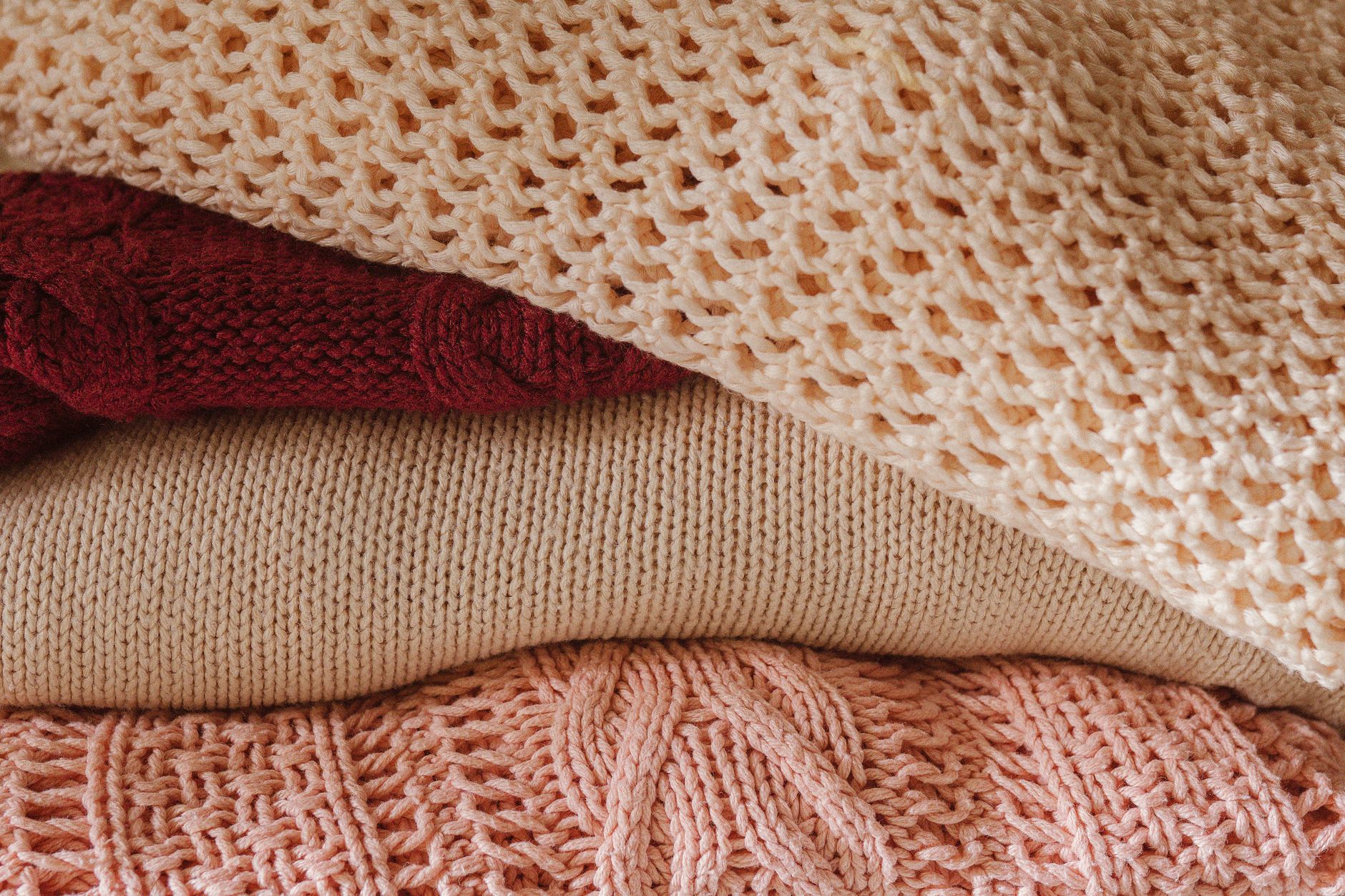 A close-up view of a cozy stack of knitted sweaters in warm shades, emphasizing texture and comfort, illustrating Short fibers, not cheap prices, are why cashmere pills