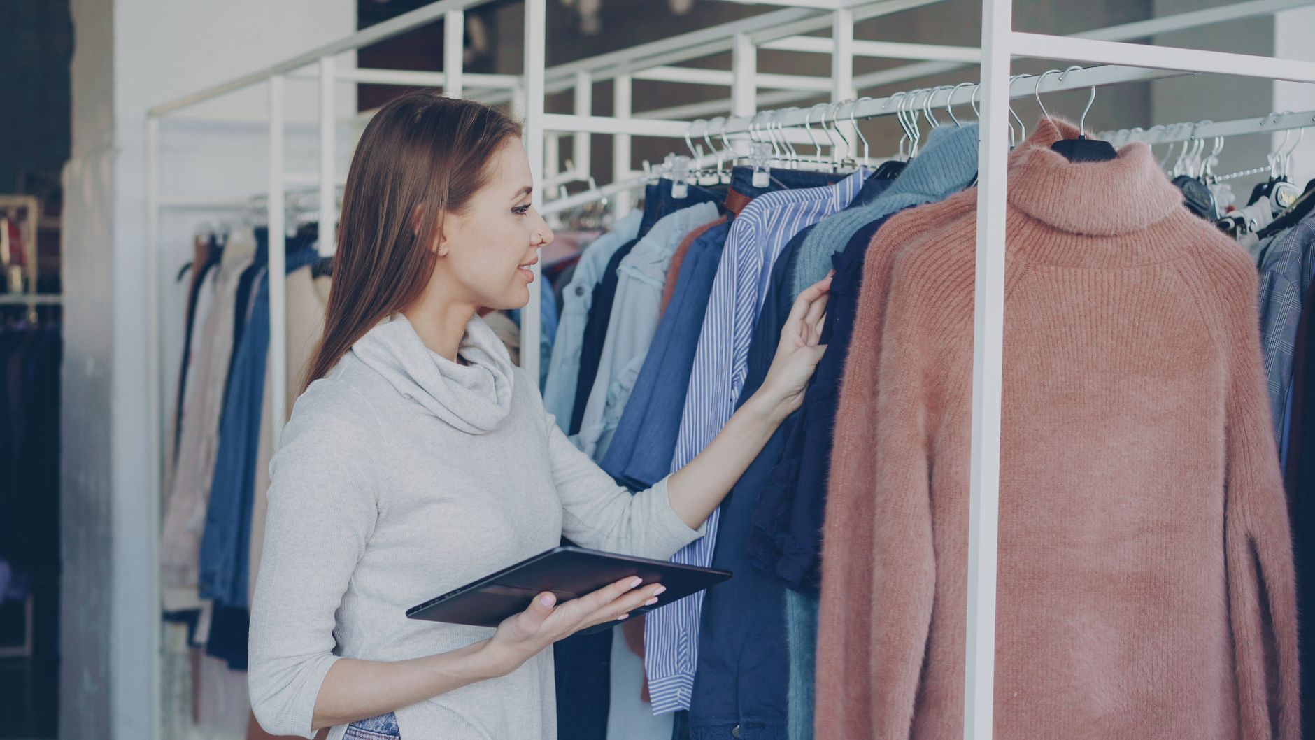 A woman browsing sweaters in a fashion retail store holding a tablet, illustrating Is cheap cashmere worth it? Run the cost per wear