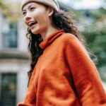 Smiling woman in a red knit sweater and warm hat walking with a friend on a city street in sweater season
