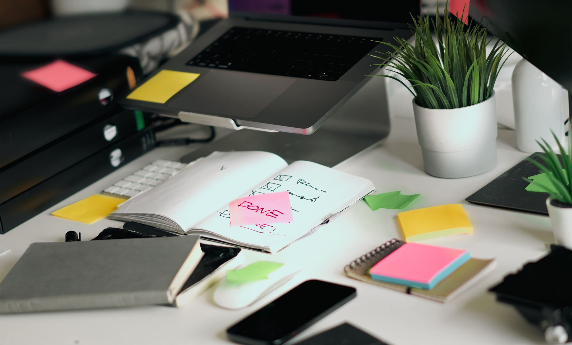 A cluttered office desk featuring a laptop, notebooks, and checklists amid colorful sticky notes, illustrating Streamlining Workflows and Processes