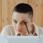 Close-up of woman with short hair applying eyeliner while looking into a mirror, illustrating Mastering the Art of Winged Eyeliner: 5 Foolproof Techniques for Every Eye Shape
