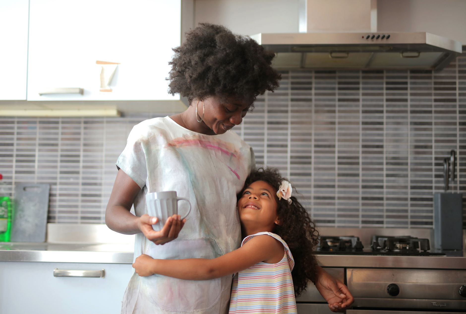Mother and daughter laughing over coffee at a kitchen table by the window