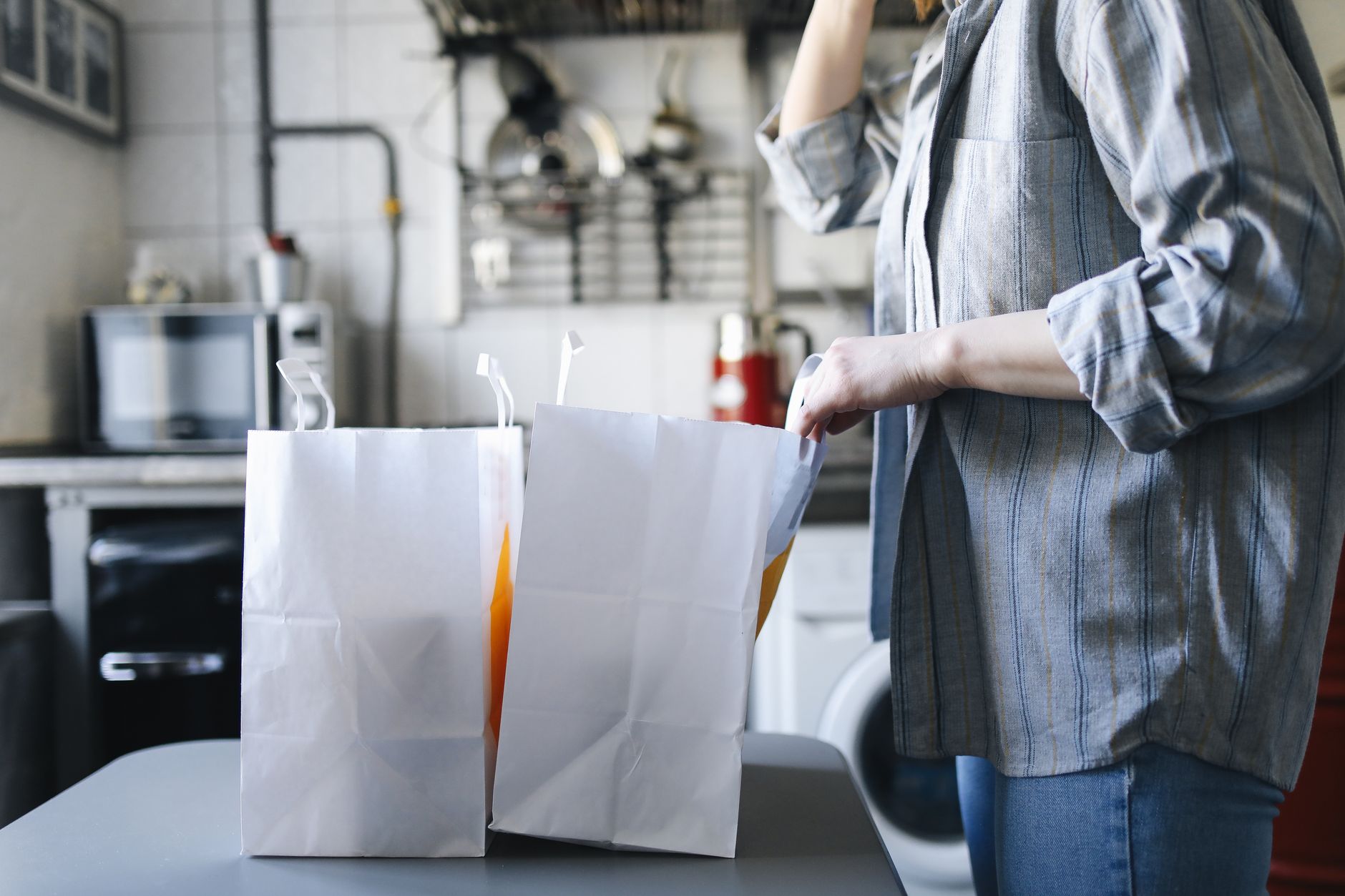 Woman in casual attire handling paper bags for delivery service in a kitchen setting, illustrating The real number from a no spend month is about $526