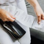 Close-up of a woman's hands managing multiple receipts taken from a black wallet, illustrating No Spend January Saves About $526. The Fix That Lasts Is Worth More