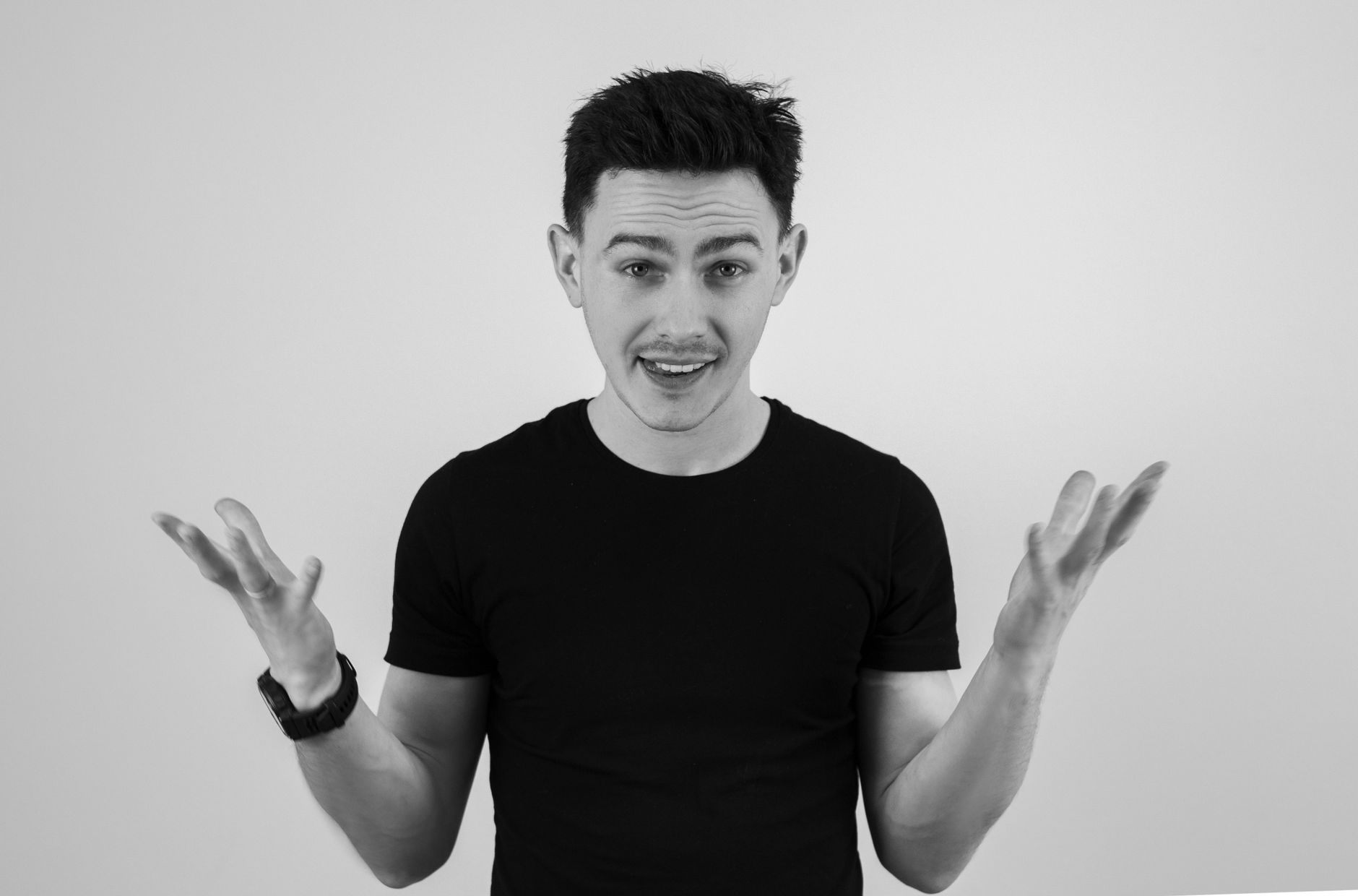 Black and white portrait of a man in a black t-shirt gesturing with open hands, illustrating II. Types of Non-Verbal Communication