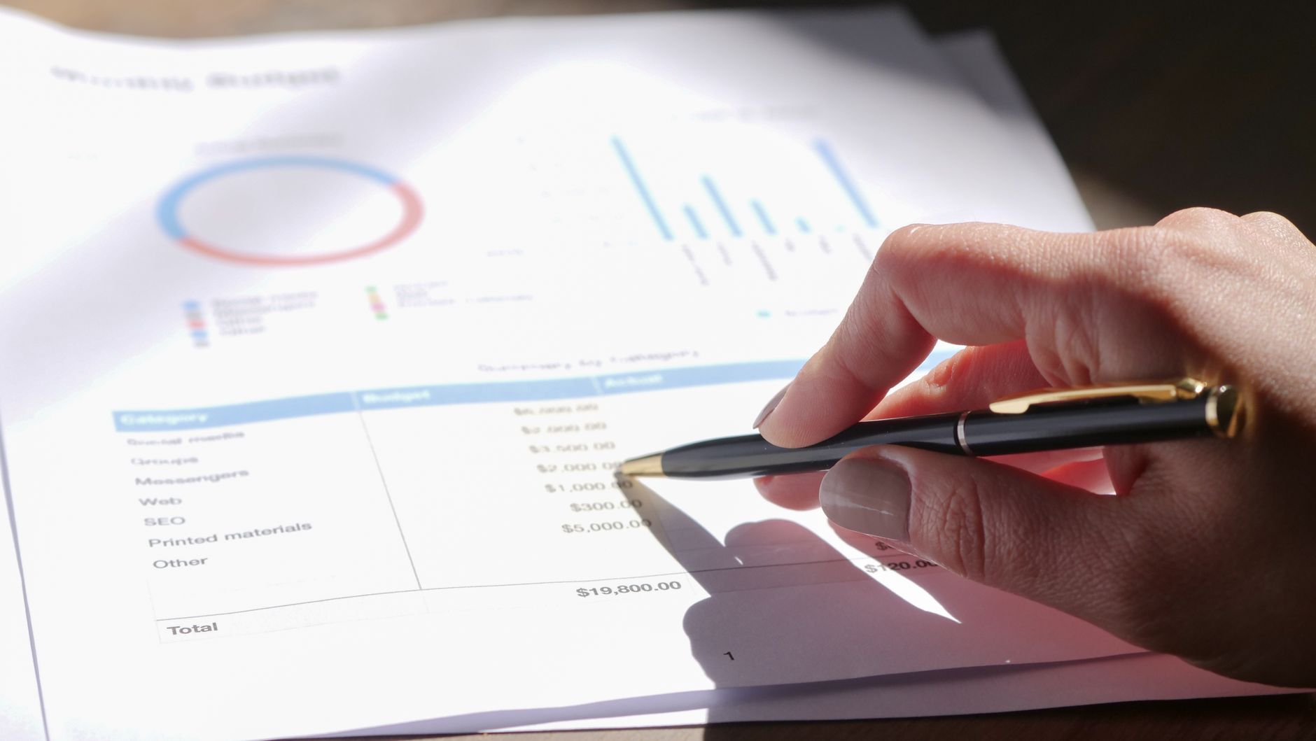 Hand holding pen, analyzing budget with charts and graph paper, illustrating Creating a Budget That Actually Works