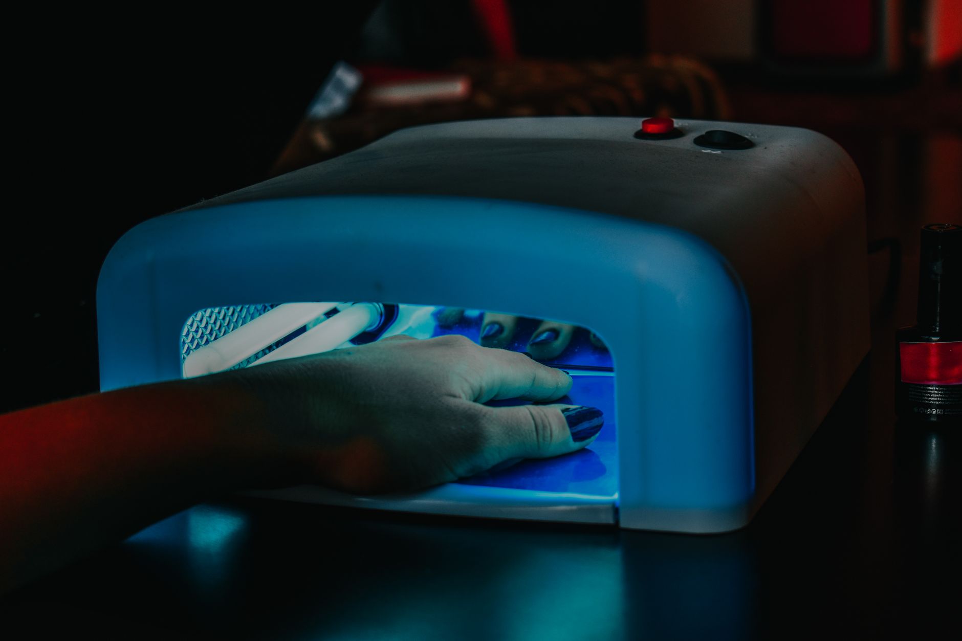 Hands under a UV nail lamp during a gel manicure, the source of the small but real UV exposure risk