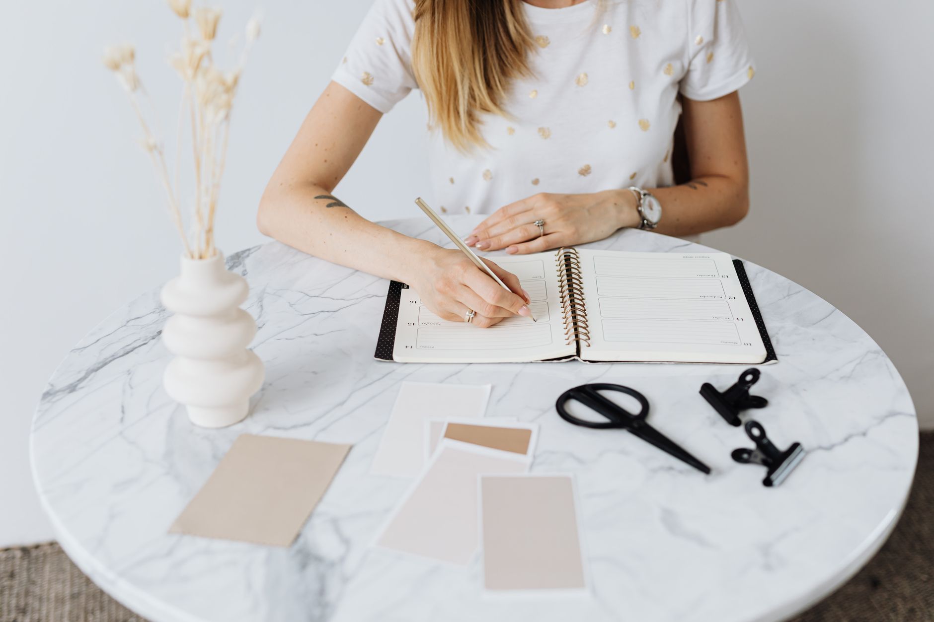 A woman writes in her planner on a marble table with stationery items, illustrating Time Management and Organization