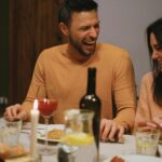A joyful couple shares laughter and affection during a cozy dinner with wine and candlelight, illustrating Valentine's Day Date Ideas: Why a $72 Climbing Class Beats a $210 Dinner