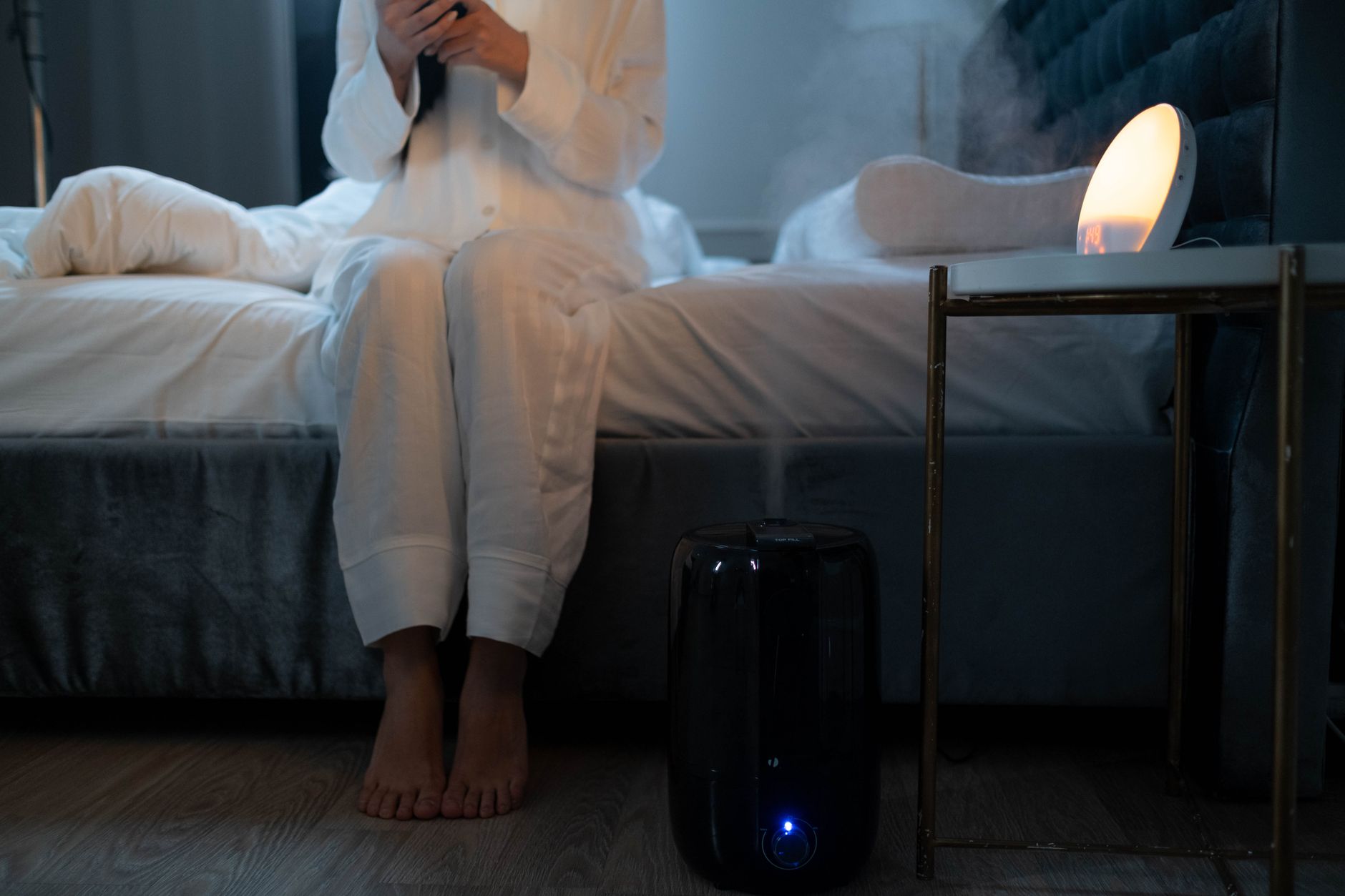 A serene bedroom scene with humidifier mist illuminating soft lighting, creating a calm atmosphere, illustrating The target is 30% to 50% indoor humidity, and more is worse